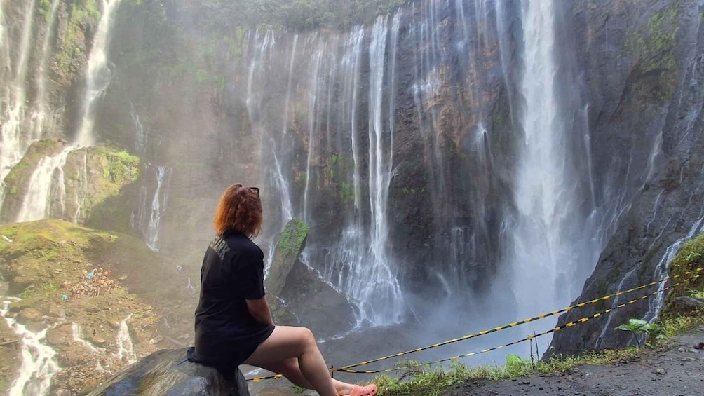A person sitting on a rock by a waterfall. 3