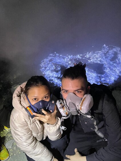 Two people wearing masks and holding devices, with a projection of a blue abstract pattern in the background. 1