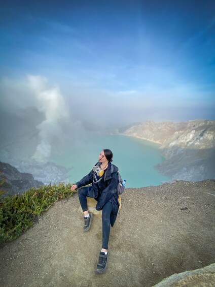 A person sitting on a rock by a lake with mountains in the background. 2
