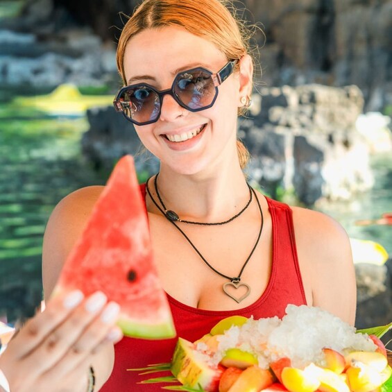 A person holding a slice of watermelon and a plate with various fruits and rice. 2