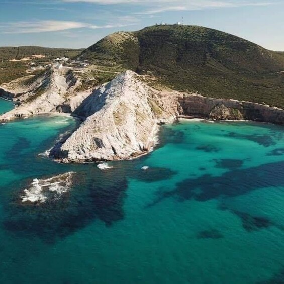 A coastal landscape with a prominent rocky outcrop surrounded by turquoise waters. 4