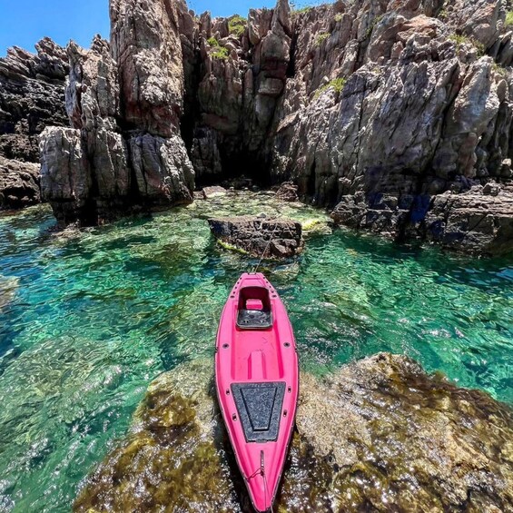 A pink kayak in clear water surrounded by rocky cliffs. 3