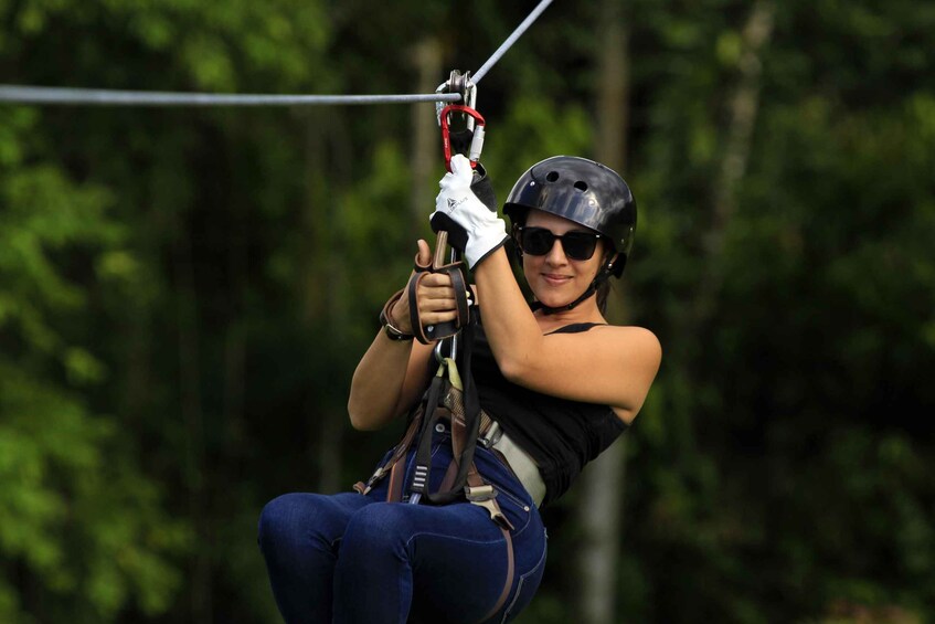 A person engaged in ziplining, wearing a helmet and harness, with trees in the background. 1