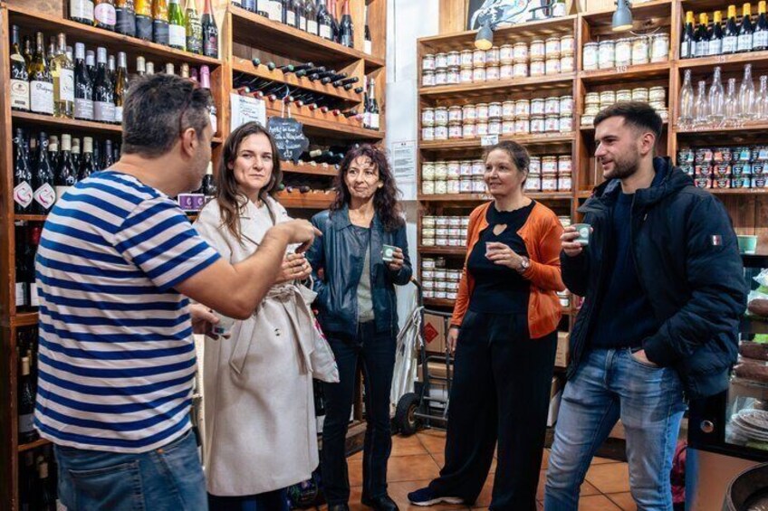 A group of people in a wine shop with shelves of bottles and jars. 4