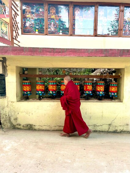 A person in traditional red robes walking past a building with colorful prayer wheels. 2