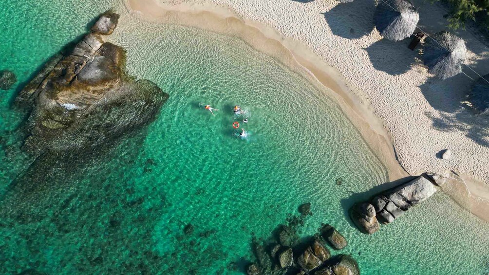 A clear turquoise sea, a sandy beach, and large rocks. 1