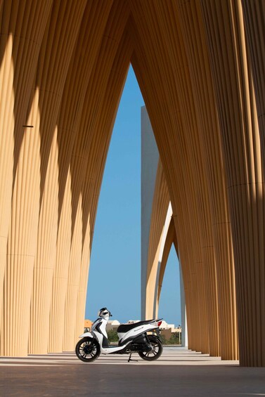 A scooter parked under a large, arched structure with a clear blue sky in the background. 2