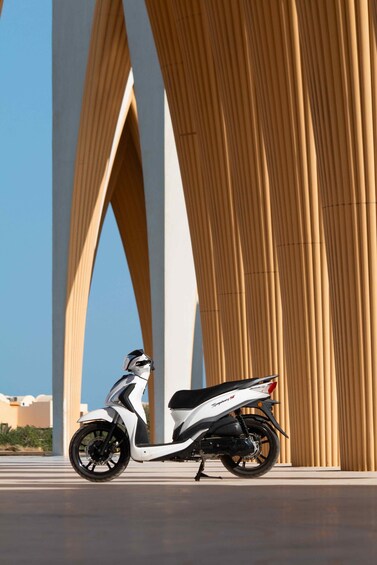 A white scooter parked in front of a modern architectural structure with large, curved columns. 4