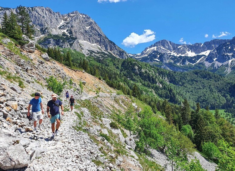 Hikers on a rocky mountain trail with snow-capped peaks in the background. 3