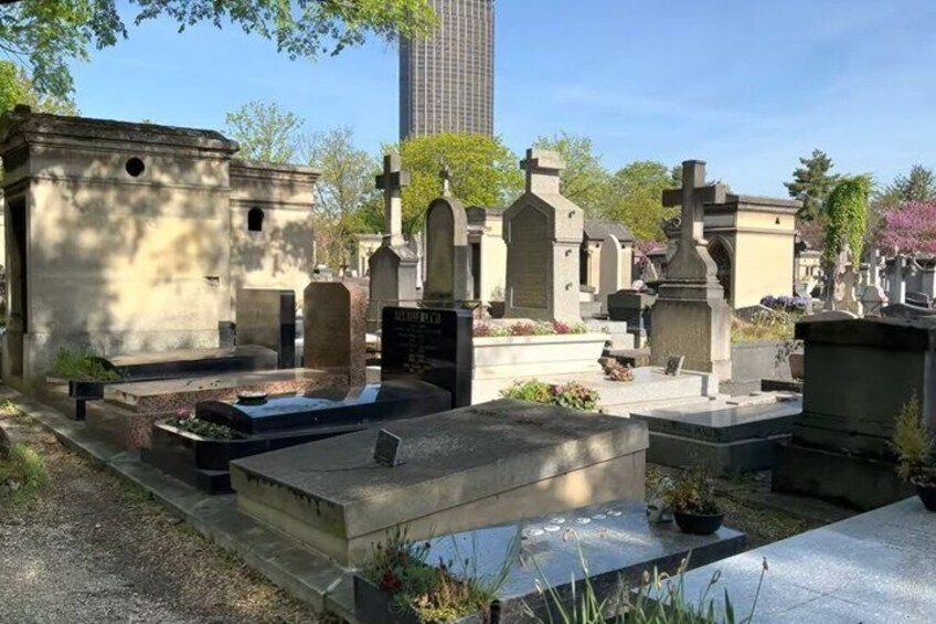 A cemetery with various headstones and tombs, surrounded by trees and a building in the background. 5