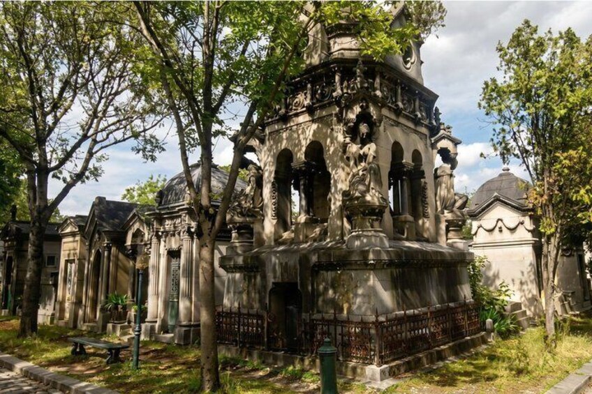 A historic building with ornate architecture, surrounded by trees and other tombs. 1