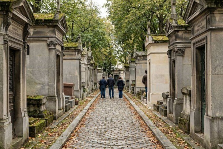 A cobblestone path lined with stone tombs and trees. 3