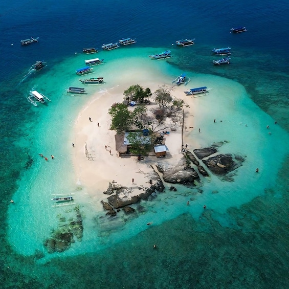 An aerial view of a tropical island with clear turquoise waters, a sandy beach, and several boats anchored around the island. 1