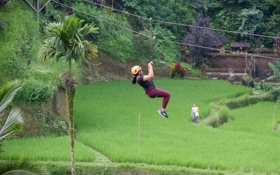 A person zip-lining over a lush green landscape with terraced fields and traditional structures in the background. 5