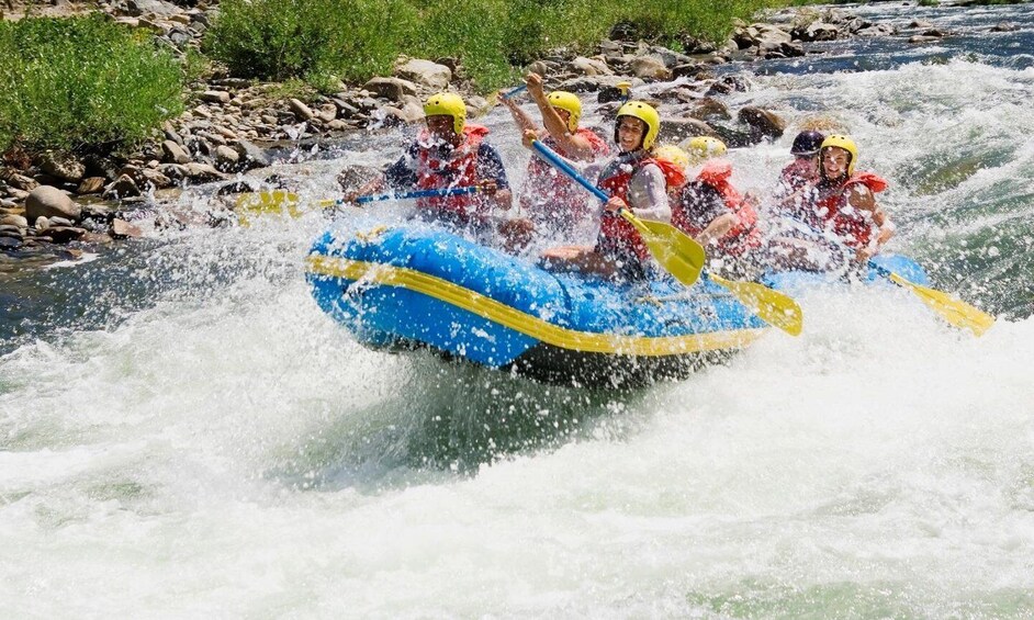 A group of people in a blue and yellow raft navigating a river with rapids. 2