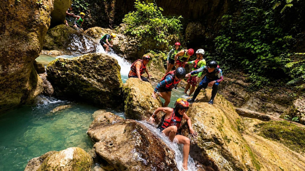 People rappelling down a rocky waterfall in a forested area. 5
