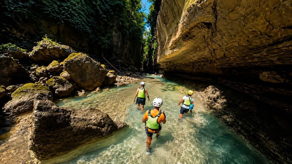 Three people wading through a clear river in a rocky canyon. 2
