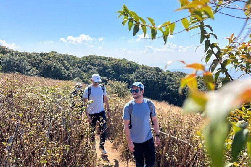 Two people hiking on a trail surrounded by dry vegetation and hills. 1