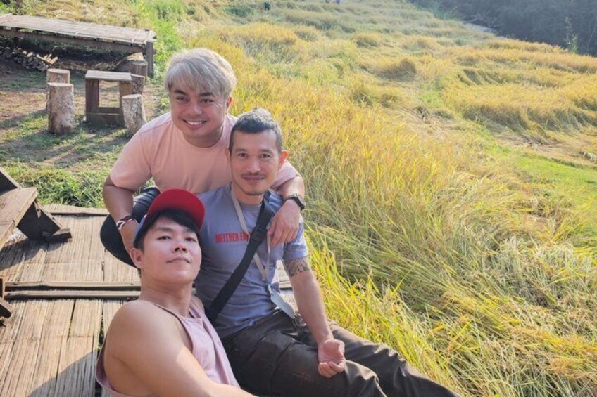 Three people sitting on a wooden deck with a grassy landscape in the background. 4