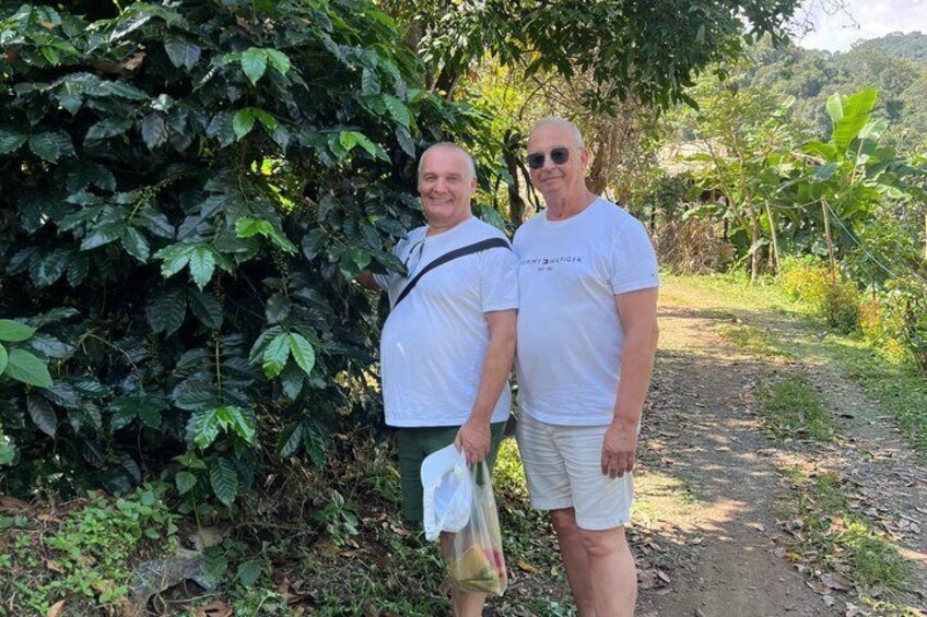 Two people standing on a dirt path with dense foliage and a hill in the background. 3