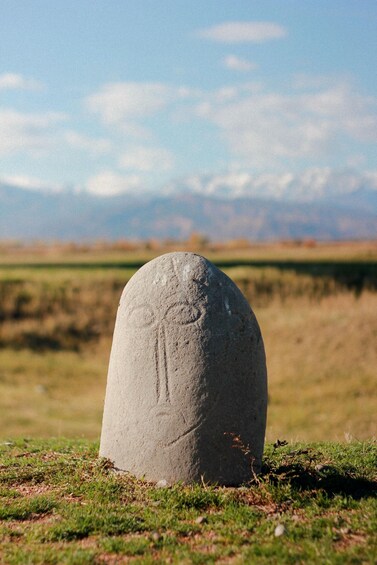 A large stone monument with carvings in a grassy field with mountains in the background. 5