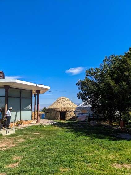 A building with large windows, a yurt, and a thatched-roof structure in a grassy area. 2