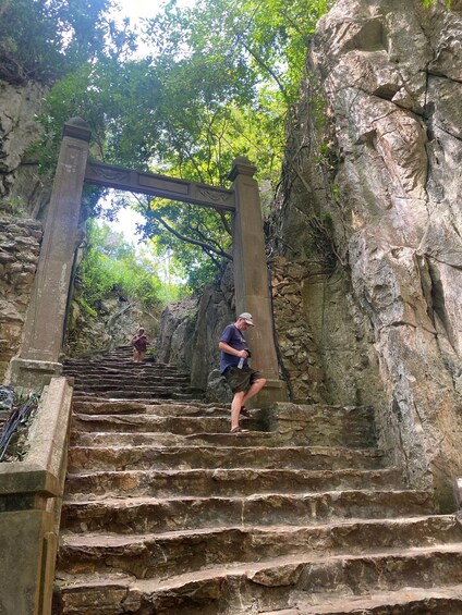 Un escalier en pierre menant à un sentier rocailleux, bordé de verdure et surmonté d’une arche en pierre. 3