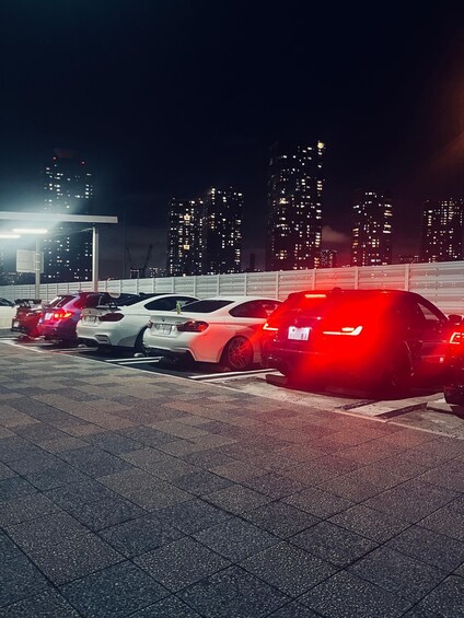 A parking lot with several cars at night, illuminated by street lights. 4