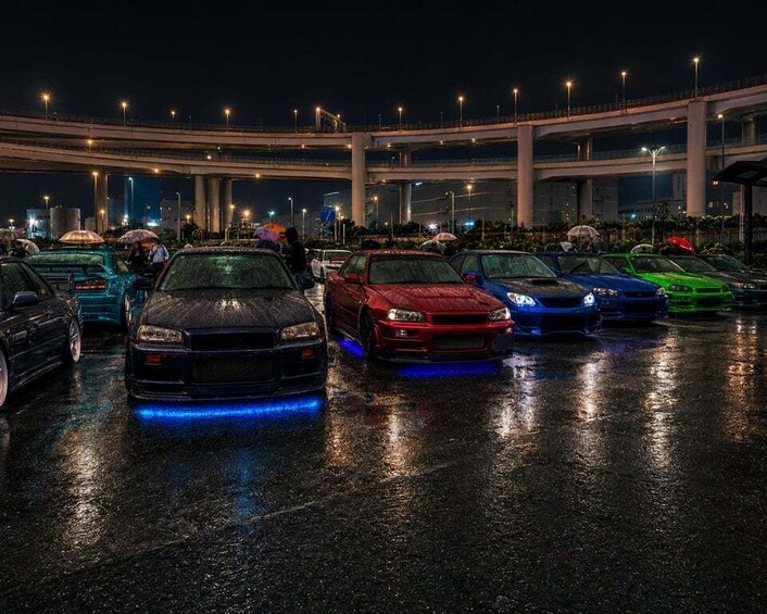 A nighttime parking lot with multiple cars and a bridge in the background. 2