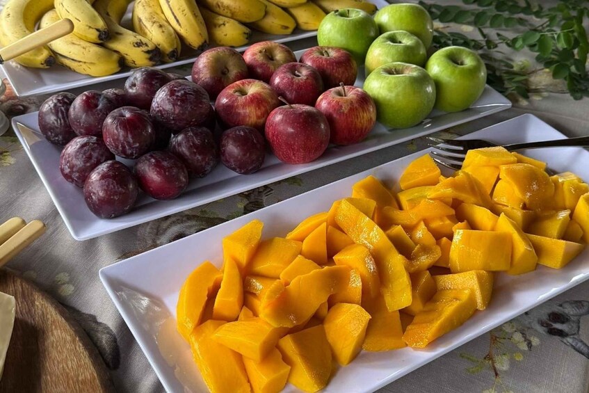 A fruit platter with bananas, apples, plums, and mangoes. 4