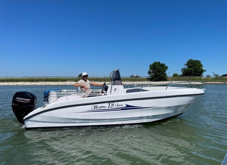 A white boat with 'Marine 18 Open' written on the side, a man in a white cap and beige shirt, and a calm water body with a clear sky. 1