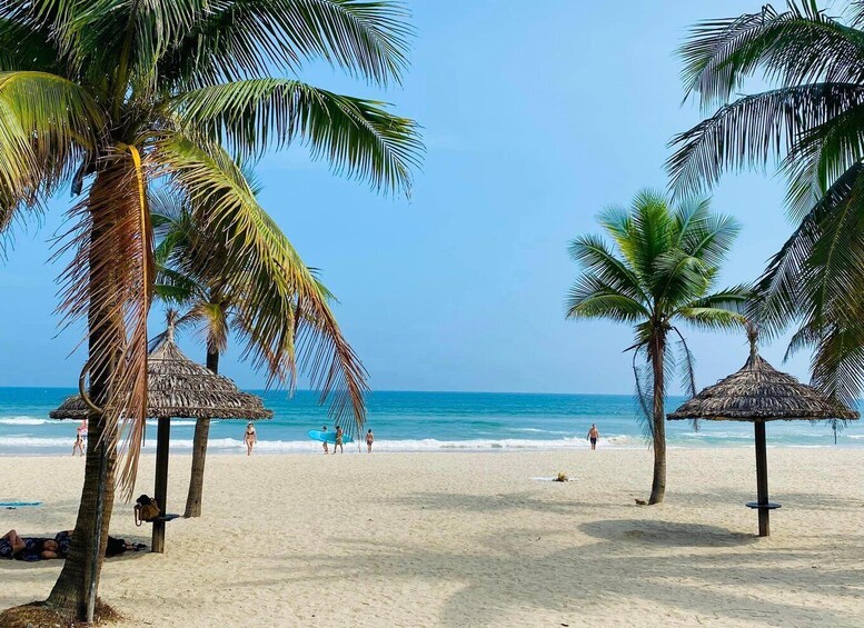 A beach with palm trees, thatched umbrellas, and people walking along the shore. 1