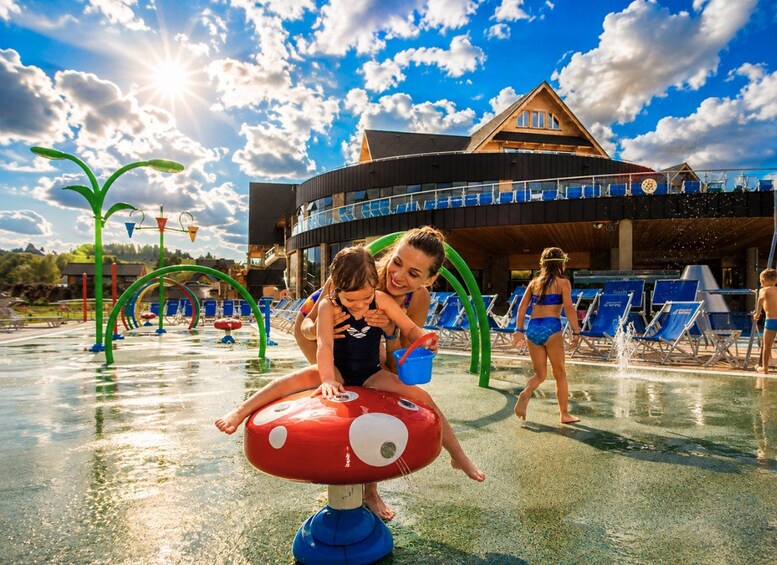 A water park with a red mushroom play structure, a building with a triangular roof, and blue lounge chairs. 5