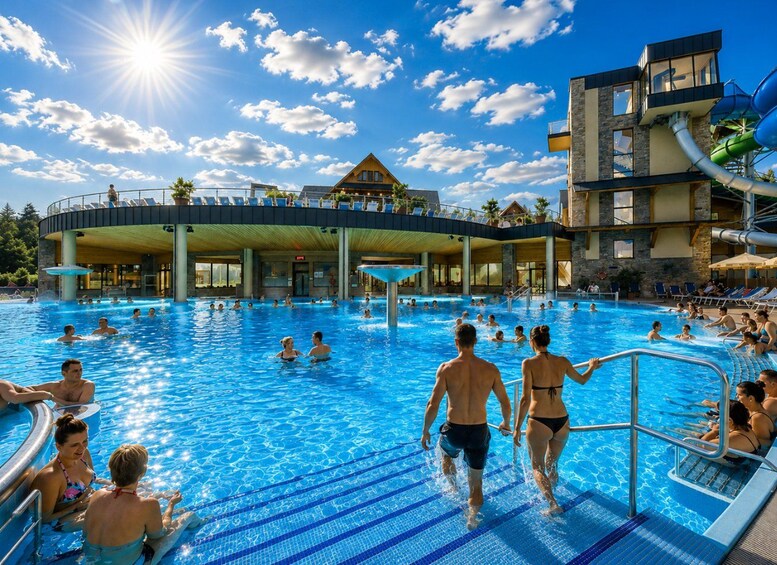 Une grande piscine extérieure où l’on peut nager et où les gens se promènent. On y trouve un bâtiment avec un toit en bois et un poste de surveillance pour les sauveteurs. 5