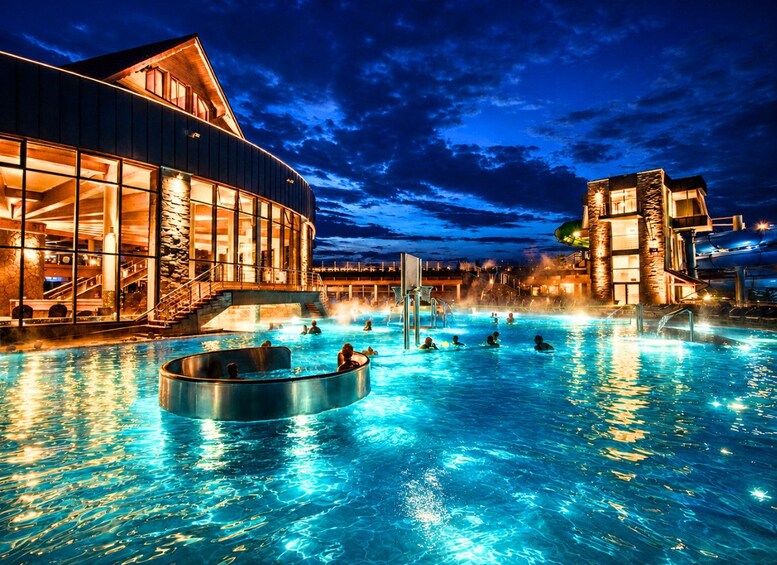 A nighttime swimming pool with people, a building with large windows, and a clear sky. 4