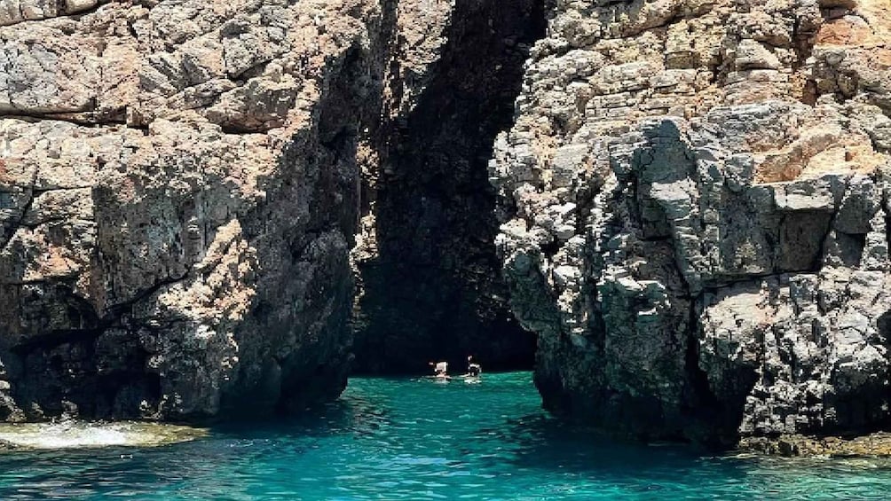 A rocky coastal landscape with a narrow water passage and two people swimming. 5