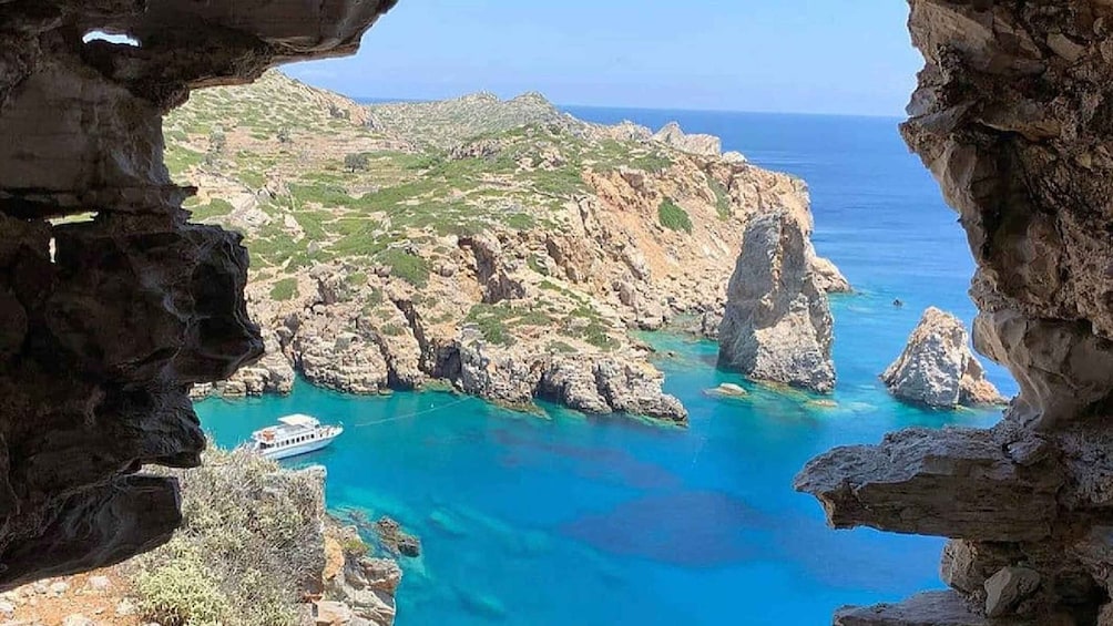 A rocky coastline with clear blue waters, a boat, and a cave entrance. 1