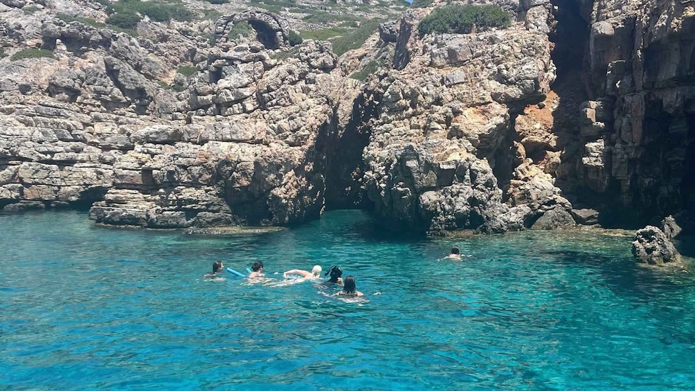 A group of people swimming in a clear blue sea surrounded by rocky cliffs. 4