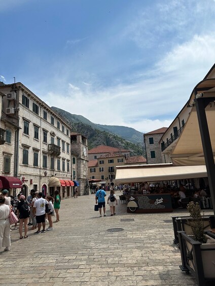 A cobblestone square with historic buildings, a clock tower, and a café. 3
