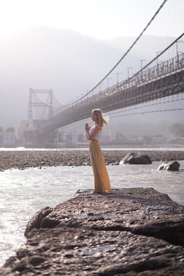 A person standing on a rock by a river with a bridge in the background. 1