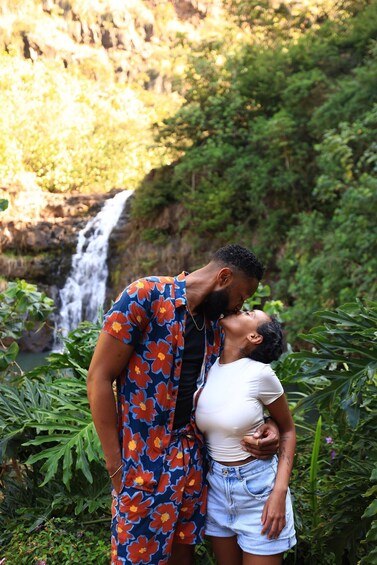 A couple embracing in a lush garden with a waterfall in the background. 5