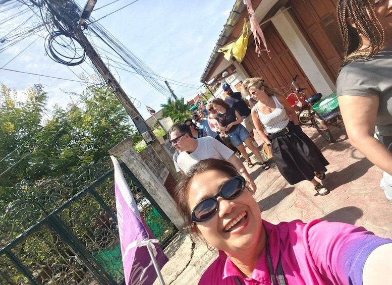 A person taking a selfie with a crowd in the background, a flag, and a building with a sign. 3
