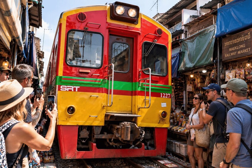 A red and yellow train with the number 1227 on the front, parked in a market area with people around it. 5
