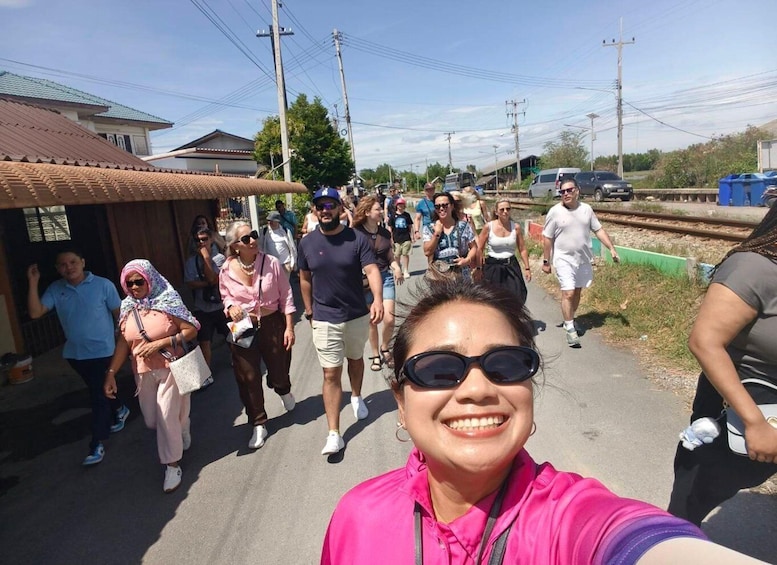 A group of people walking on a paved path beside a railway track. 2