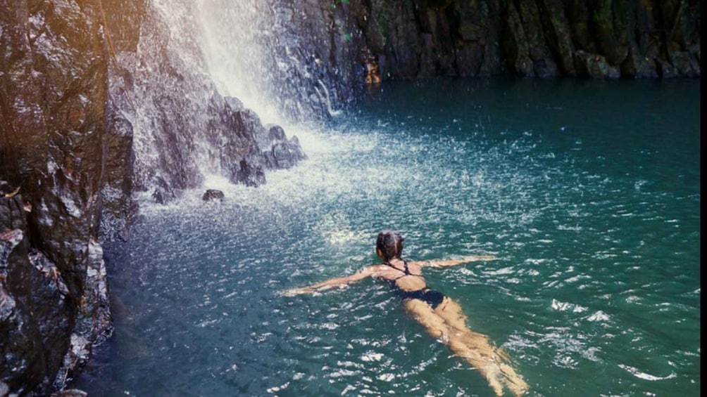 A person swimming in clear water near a waterfall. 5