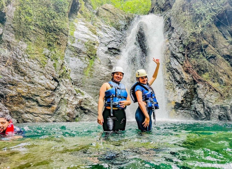 Two people in water with a waterfall in the background. 1