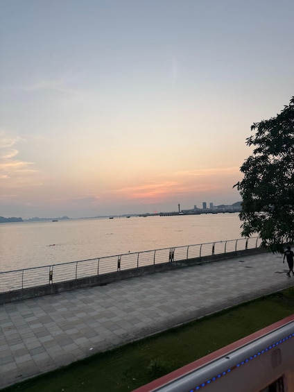 A riverside walkway with a railing, a tree, and a distant city skyline. 4