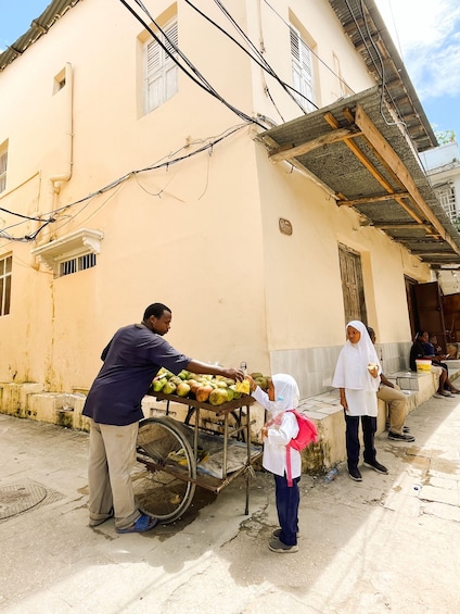 A street vendor selling fruits in front of a building with a tiled roof and a person standing nearby. 3