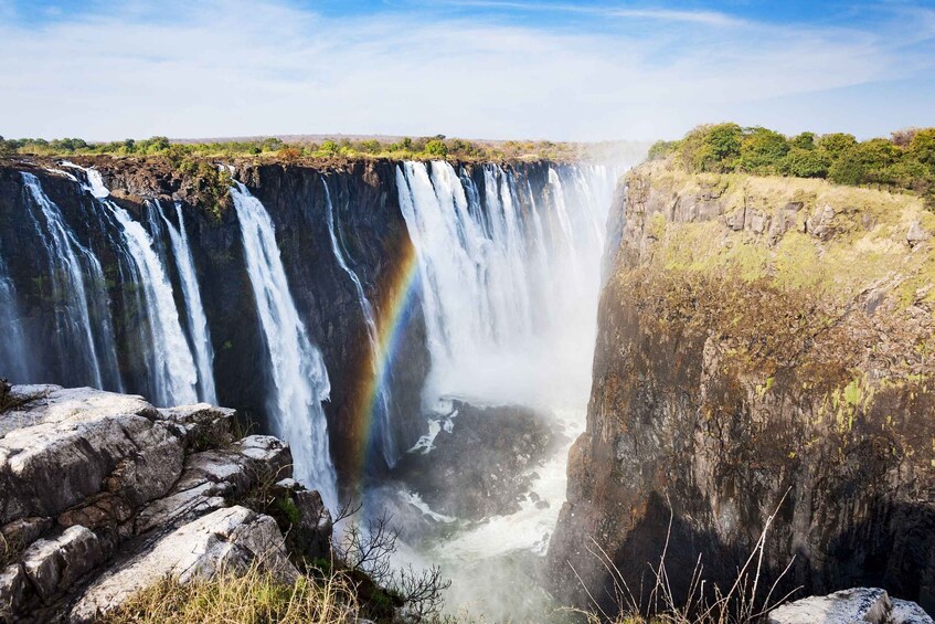 A large waterfall with a rainbow, surrounded by rocky terrain and sparse vegetation. 3
