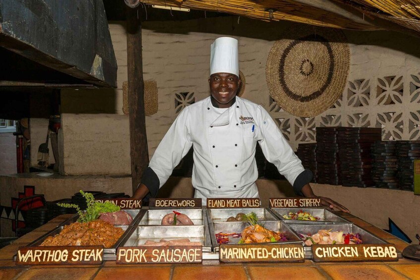 A chef in a kitchen with labeled food stations for various dishes like steak, sausage, and chicken. 2